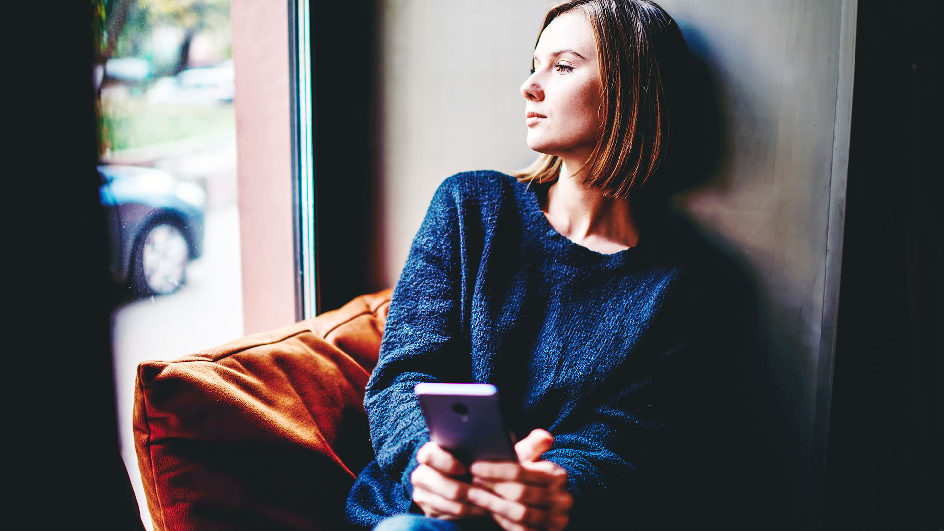 Woman looking out the window with phone in hand